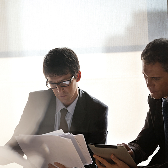 Two men looking at paperwork and tablet